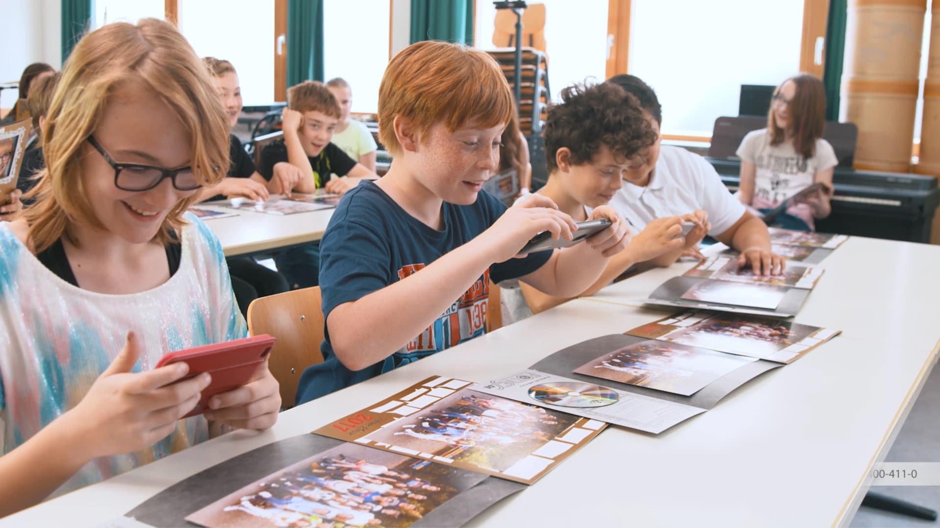 Schulfotograf fotografiert eine Klasse in einer Aula, alle lachen entspannt in die Kamera.
